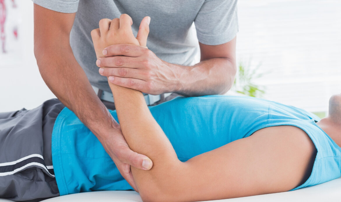 Physical therapist moves patient's elbow area and holds patient's wrist checking for tendonitis pain while patient is on medical table.