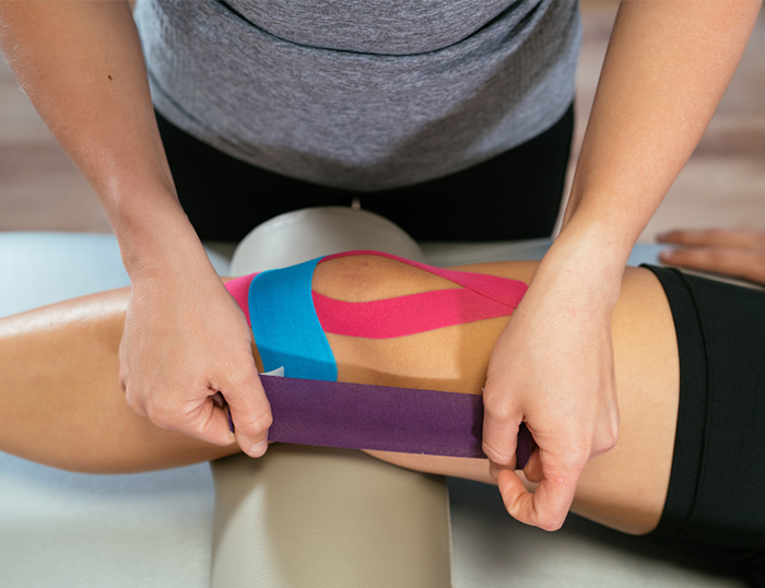 physical therapist applies Kinesio tape to an athlete's knee to prevent Athletic Injury