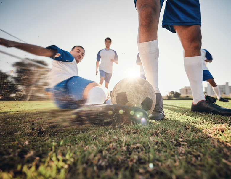 Athletic soccer player does a slide tackle to steal the ball while opposite team player intercepts the play.