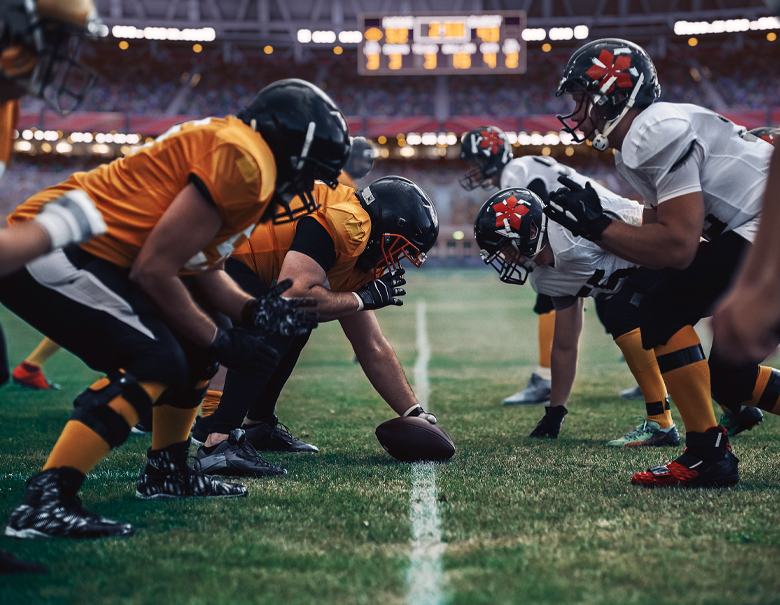 Football teams stand opposite each other while standing at the line of scrimmage getting ready to start the game