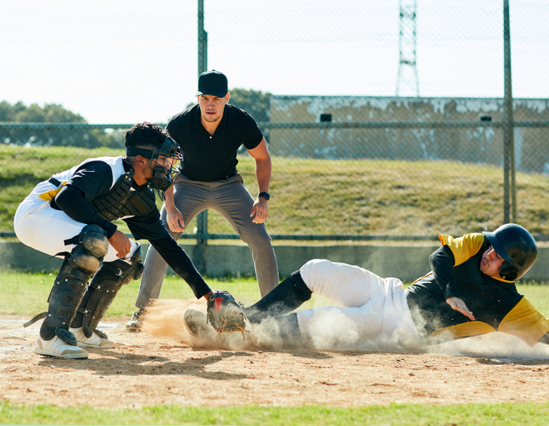 Baseball player sliding into home plate while catcher attempts to catch the ball