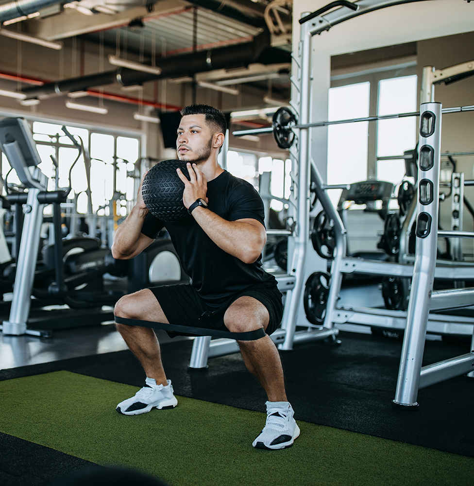 man doing squats with restriction band while holding exercise medicine ball