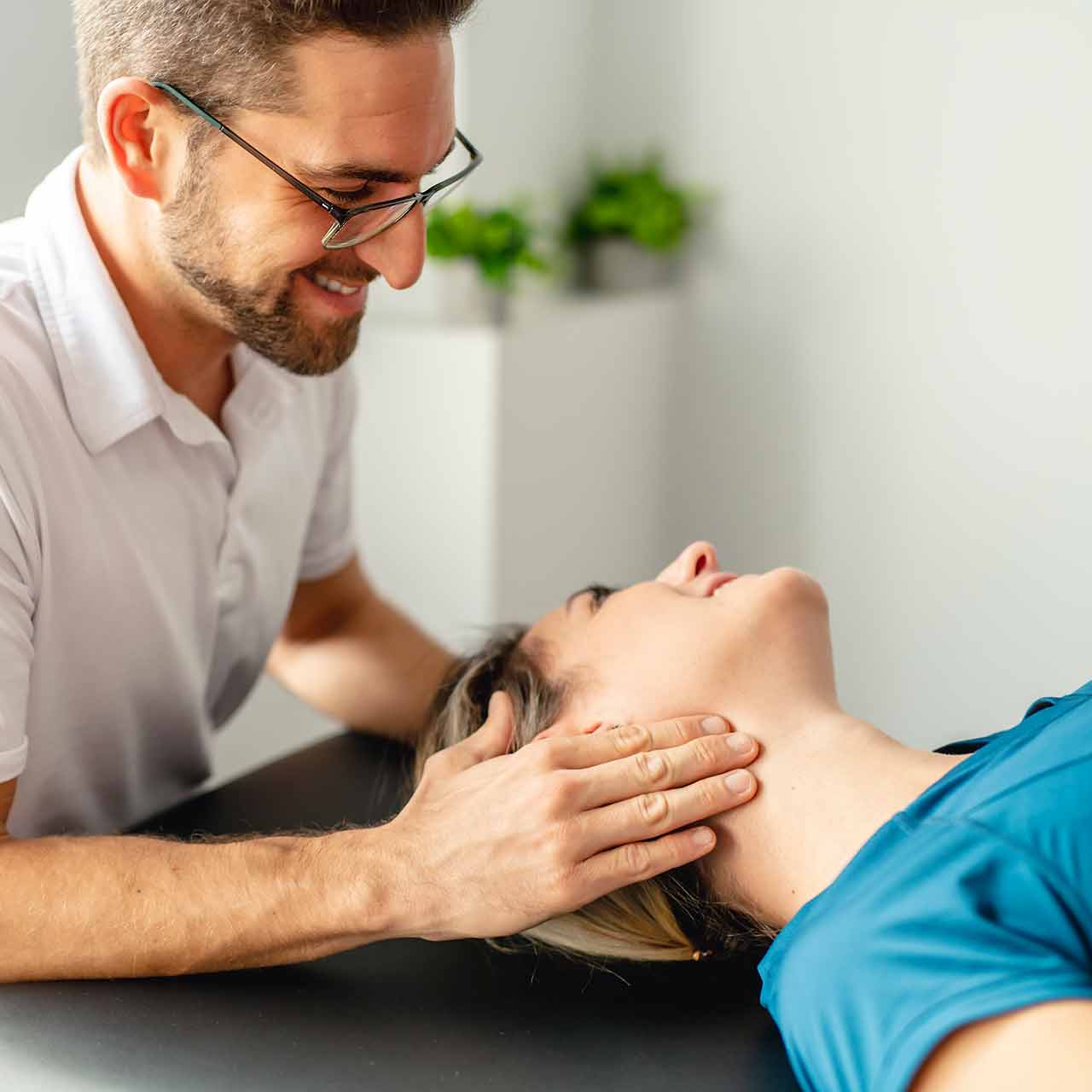 A male physical therapists checks the neck of a female patient