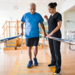 Elder man doing Physical Therapy balance exercise on parallel bars with the help of a female physical therapist