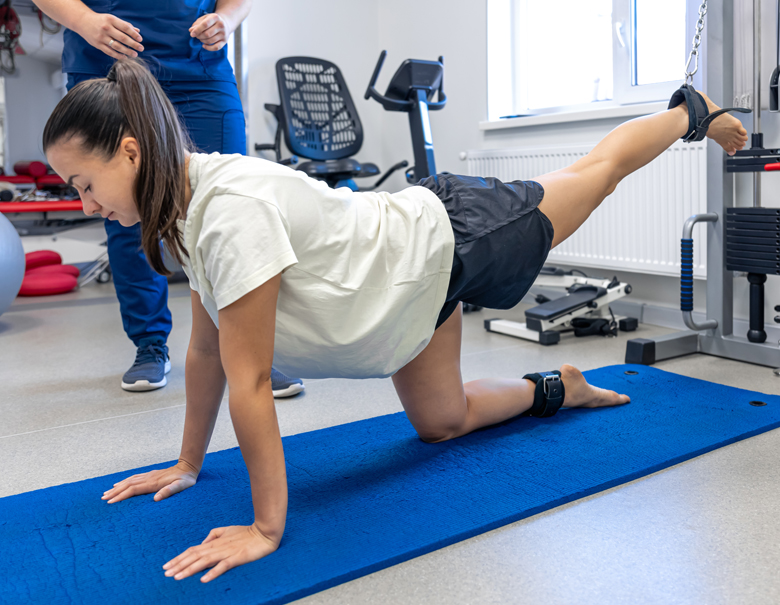 A female patient does post operative rehab leg raise exercises with the assistance of a male physical therapist