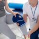 A male physical therapist holds the leg of a female patient with a knee compression sleeve.